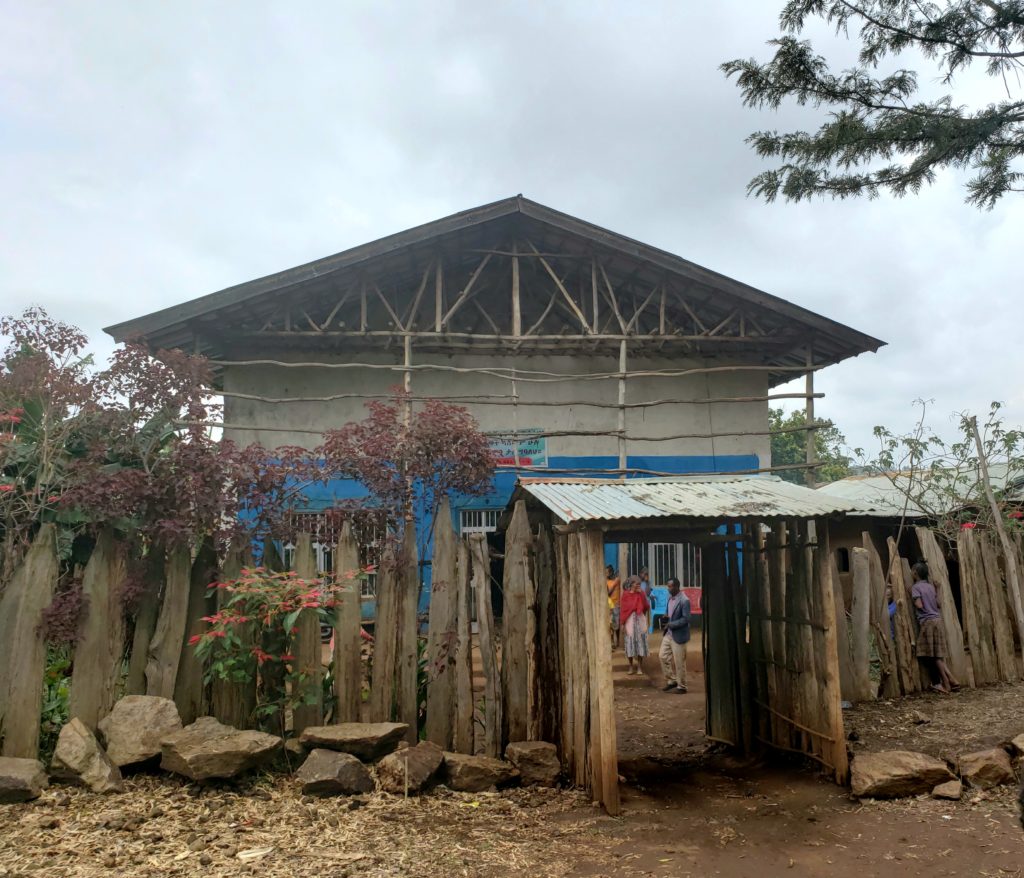 A building with people beyond a wooden fence and archway