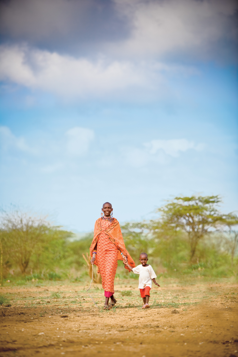 A person walking with a child through a field in Kenya