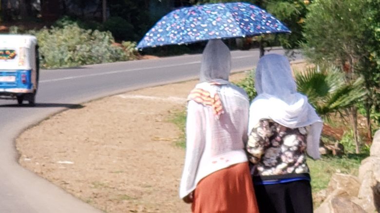 Two women walking on a road while carrying a blue and multicolored-speckle umbrella