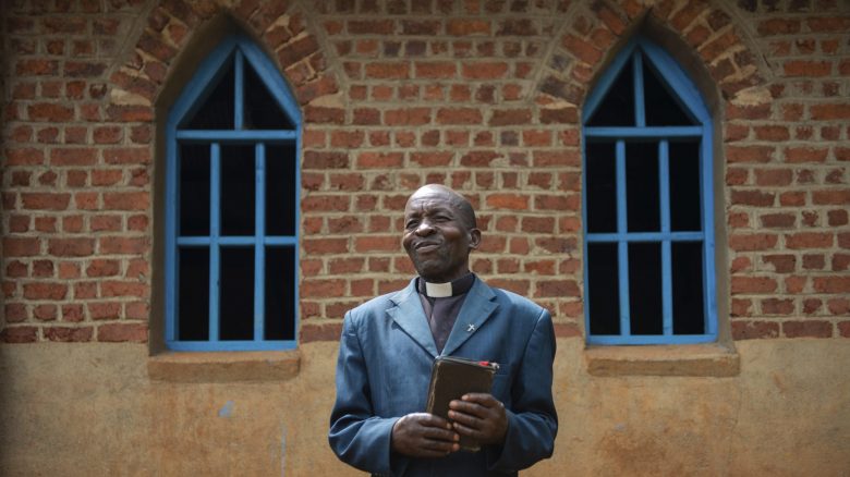 Pastor Mutsuva Vyahera Tadel, 65, poses for a portrait in front of the church in Kiwata, Democratic Republic of Congo, on 12 December 2021. Tadei has been the pastor in charge of the CBCA parish in the village of KIWATA for eight years now, where Tearfund supports the food security agriculture and community empowerment project through the AVEC programme. He says, 'Before the project started, we were farming just to eat, the crops were not enough to allow us to sell some and consume some. But since the project started, we are able to farm better, the crops are enough to consume and market.' Tearfund Canada continues to support several training and outreach programmes, with the help of CBCA, in the Democratic Republic of Congo in order to assist vulnerable communities out of poverty.