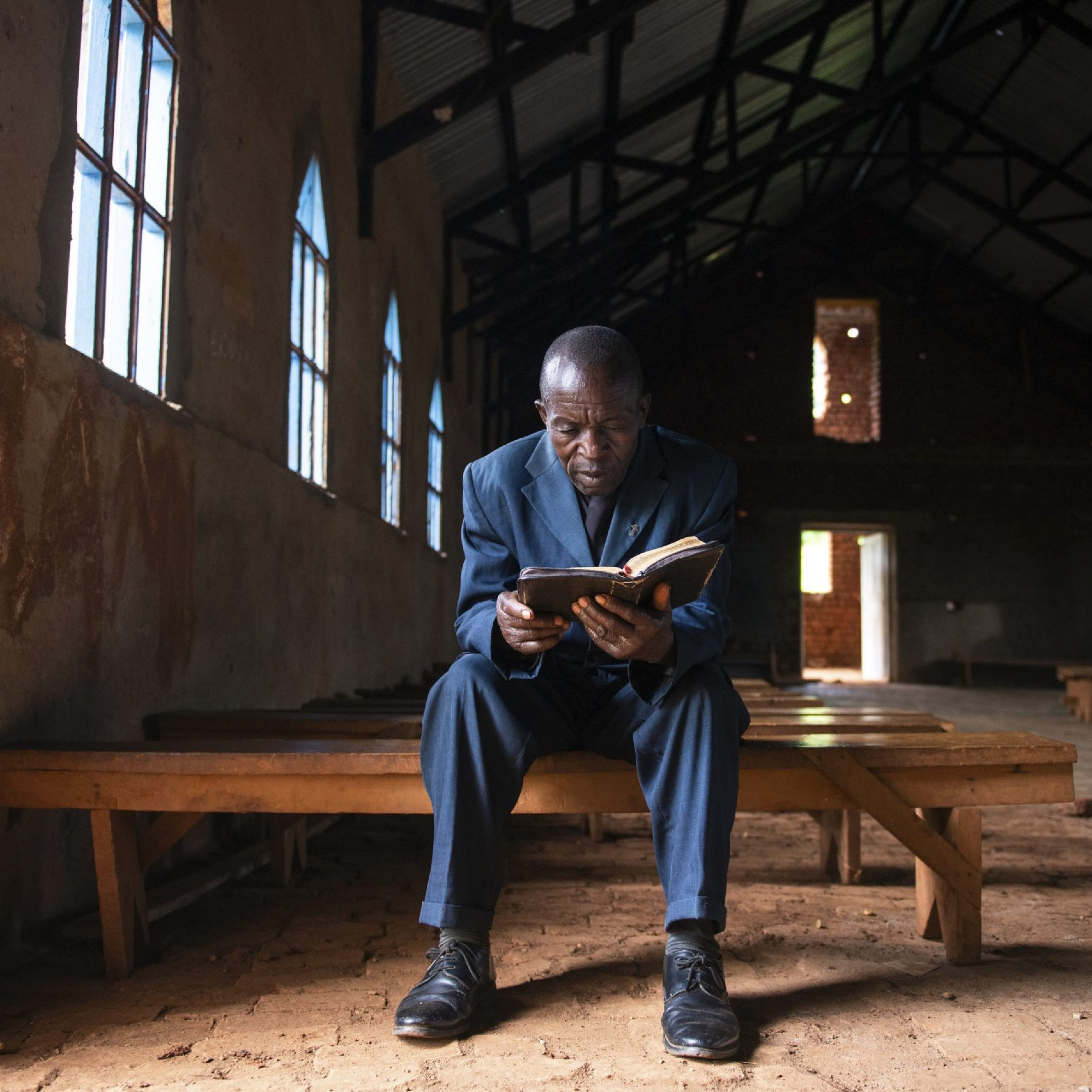Pastor Mutsuva Vyahera Tadel, 65, reads from the bible in the church in Kiwata, Democratic Republic of Congo, on 12 December 2021. Tadei has been the pastor in charge of the CBCA parish in the village of KIWATA for eight years now, where Tearfund supports the food security agriculture and community empowerment project through the AVEC programme. He says, 'Before the project started, we were farming just to eat, the crops were not enough to allow us to sell some and consume some. But since the project started, we are able to farm better, the crops are enough to consume and market.' Tearfund Canada continues to support several training and outreach programmes, with the help of CBCA, in the Democratic Republic of Congo in order to assist vulnerable communities out of poverty.