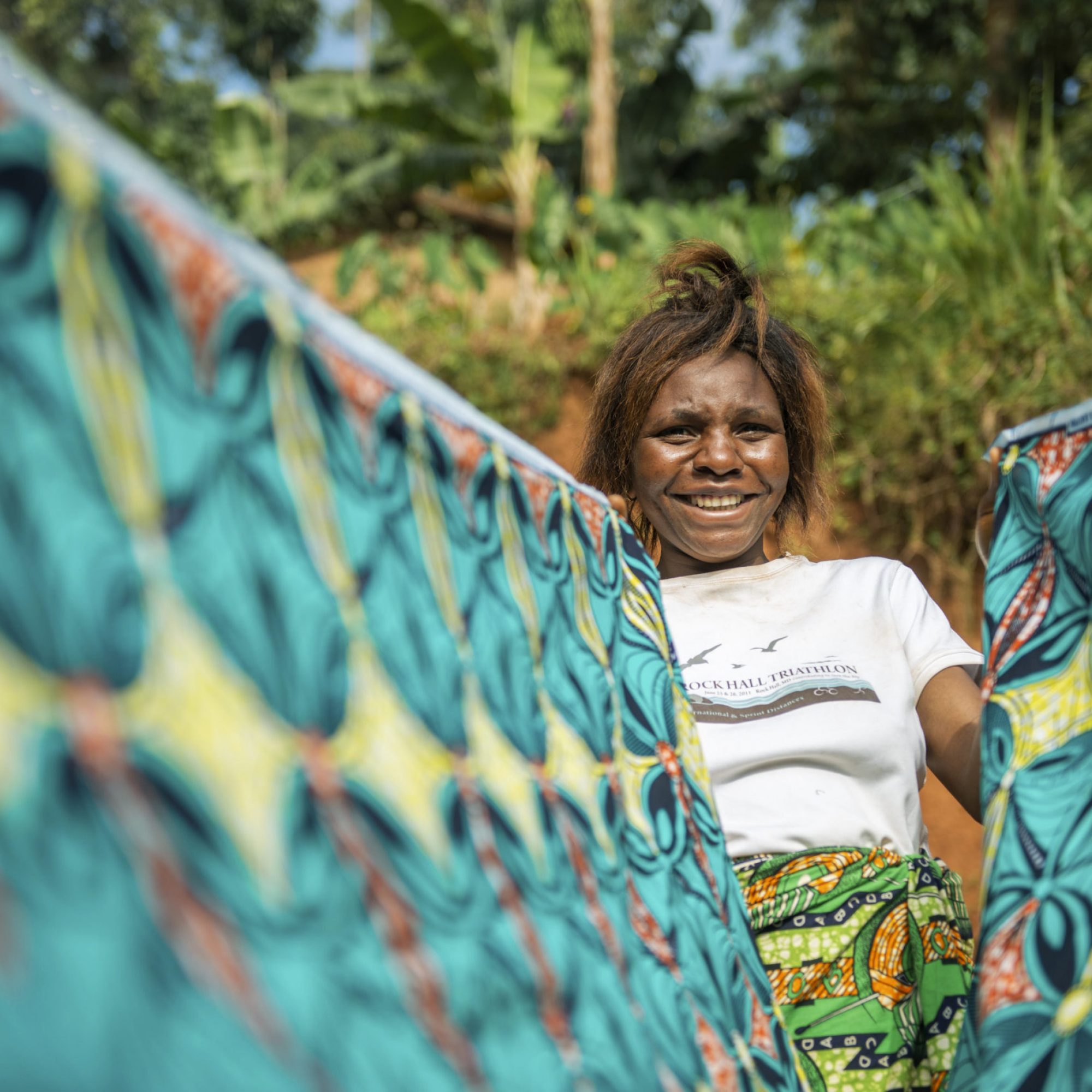 Masika Sivenfire, 24 years old and the mother of 4, poses for photograph as she holds up the material she is using to make a dress for a customer in her village Amini Yesu, Democratic Republic of Congo, on December 13 2021. Beneficiary of the loans in the AVEC group, Masika SIVENDIRE, bought a machine to create a secondary income generating activity to support her family.  She says, 'before, I used to go to the fields every day, but since I took part in the programme, I have been able to pay for a sewing machine and thanks to this profession of dressmaker that I practice, I manage to earn some money to make my weekly contributions to the group.' Tearfund Canada continues to support several training and outreach programmes, with the help of CBCA, in the Democratic Republic of Congo in order to assist vulnerable communities out of poverty.