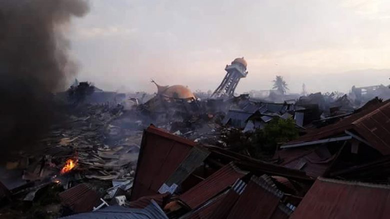 The after-effects of an earthquake, with pieces of tin, smoke, and a many collapsed buildings