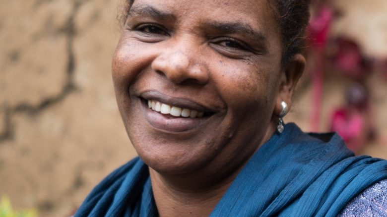 A woman wearing a blue scarf and smiling at the camera. Mamitu is from a self-help group